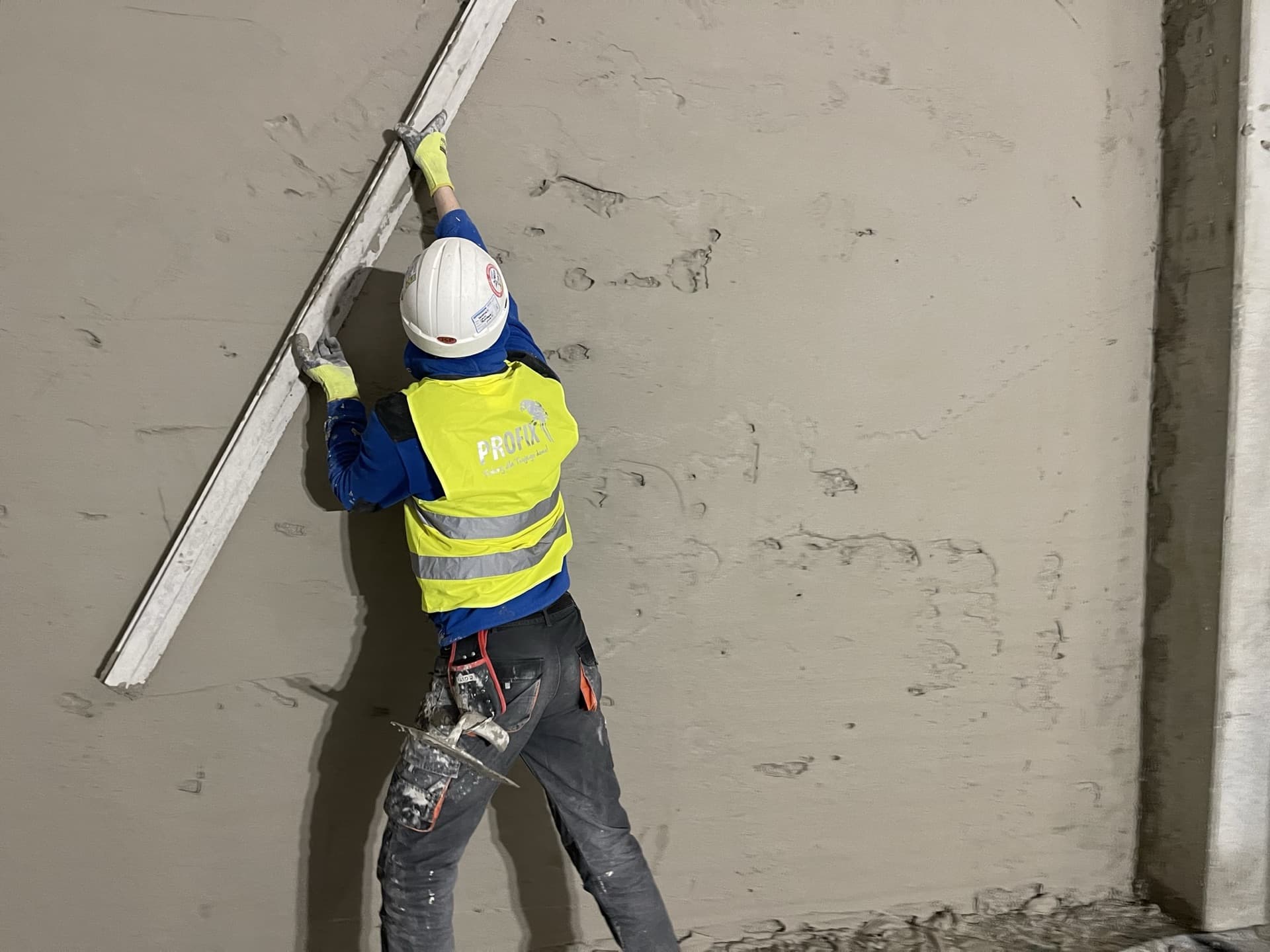 Pracownik PROFIX w hełmie i kamizelce w trakcie tynkowania